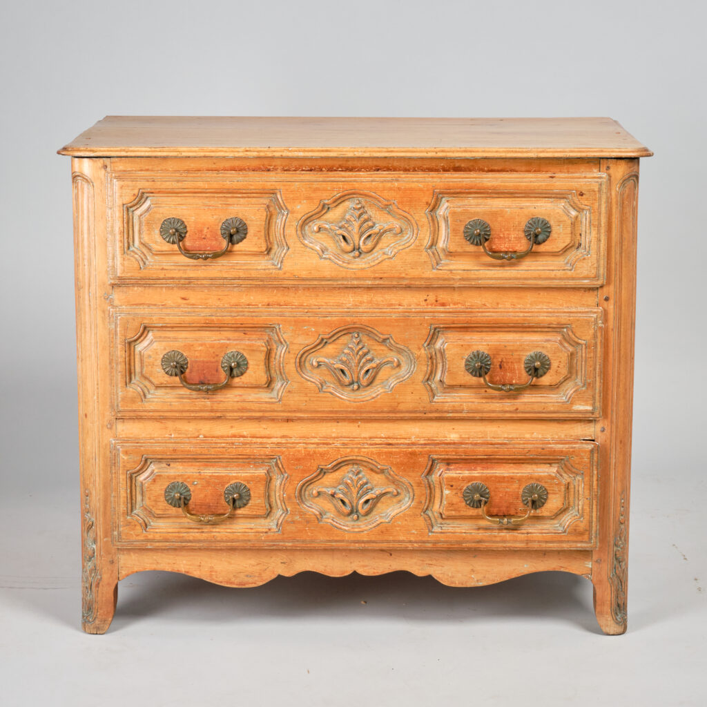 An impressive Louis XIII commode with palmette as featured in Palardy's "The Early Furniture of French Canada", plate 459. This piece has a "flat three-drawer façade with small moulded and shaped panels derived from Dauphine or Lyonnais". The drawer pulls which appear to be the original are mounted on raised panels with carved decorative trim around them. Lapped and moulded drawer fronts. There are carved floral decorations at the base of each front corner. Front and sides in pine, top in birch. Refinished. Québec, late 18th century.