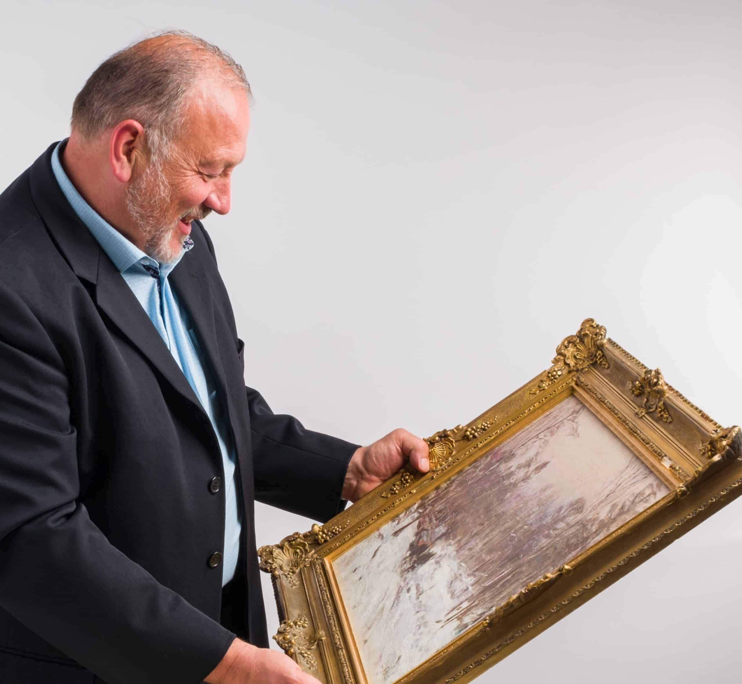 Robin Pridham, Pridham's President, examining a P. Franklin Brownell oil on canvas.